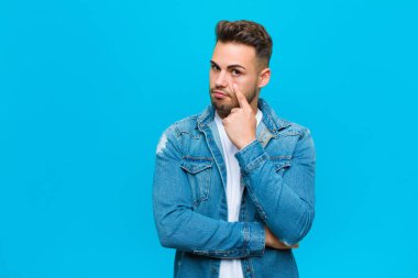 Genç İspanyol adam sana göz kulak oluyor, güvenmiyor, izliyor ve mavi arka plana karşı tetikte.