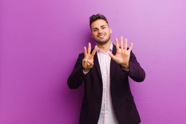 Genç İspanyol adam gülümsüyor ve arkadaş canlısı görünüyor, 8 ya da 8 numarayı gösteriyor, elleri önde, geriye doğru sayıyor.