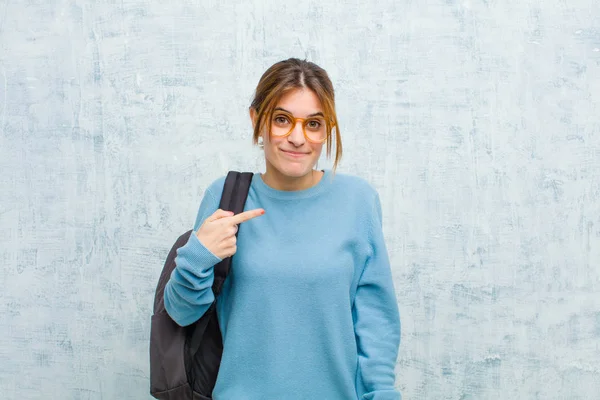 young student woman looking proud, confident and happy, smiling and pointing to self or making number one sign against grunge wall background