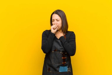 Kuaför kadın boğaz ağrısı ve grip belirtileriyle hasta, ağzı turuncu arka planda öksürüyor.