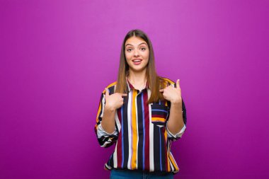 genç güzel kadın mutlu, şaşırmış ve gururlu, mor arka plan karşı heyecanlı, şaşkın bir görünüm ile kendini işaret
