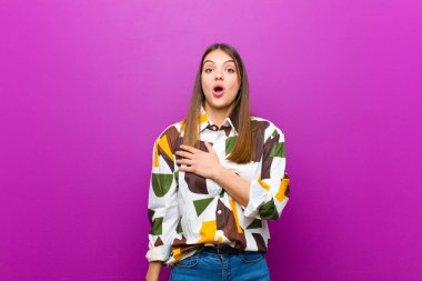 genç güzel kadın şok duygu ve şaşırmış, gülümseyen, kalp el alarak, bir olmak için mutlu ya da mor arka plan karşı şükran gösteren