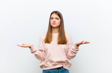 Şaşkın, şaşkın ve stresli görünen genç bir kadın, farklı seçenekler arasında merak ediyor, beyaz arka planda belirsizlik hissediyor.