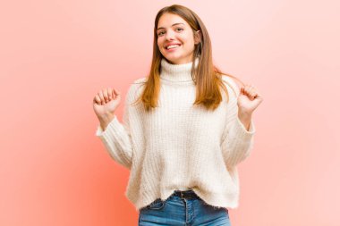 Genç ve güzel bir kadın son derece mutlu ve şaşırmış görünüyor, başarıyı kutluyor, bağırıyor ve pembe arka plana atlıyor.