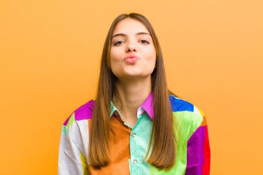 Genç, güzel bir kadın dudaklarını birbirine bastırıyor. Sevimli, eğlenceli, mutlu, sevimli bir yüz ifadesiyle. Düz bir arkaplanda izole edilmiş bir öpücük yolluyor.