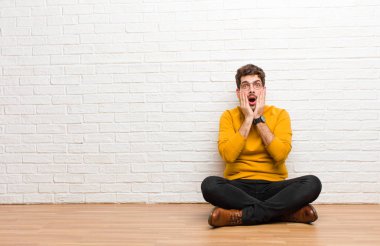 Genç yakışıklı adam tuğla duvar dokusuna karşı evde oturuyor.