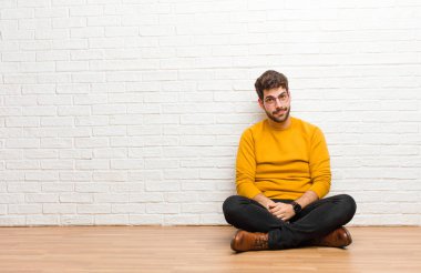 Genç yakışıklı adam tuğla duvar dokusuna karşı evde oturuyor.