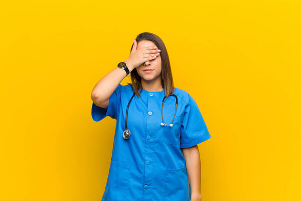 covering eyes with one hand feeling scared or anxious, wondering or blindly waiting for a surprise isolated against yellow wall