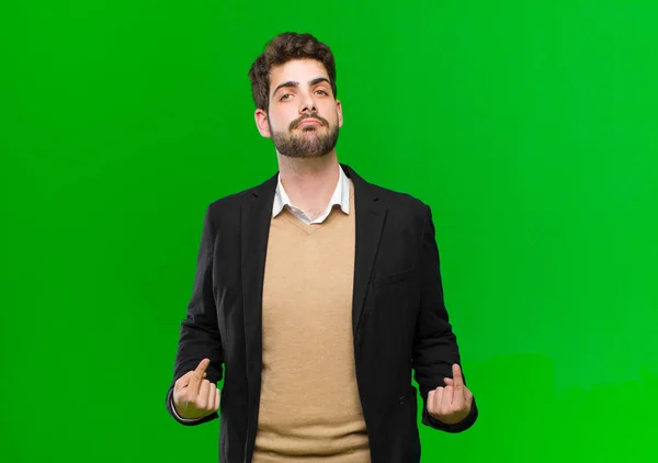 young businessman looking proud, arrogant, happy, surprised and satisfied, pointing to self, feeling like a winner against green background