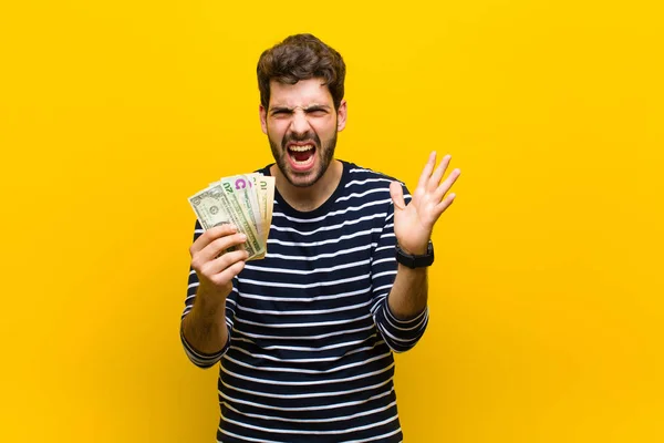 Jonge knappe man met dollarbiljetten tegen oranje backgrou — Stockfoto