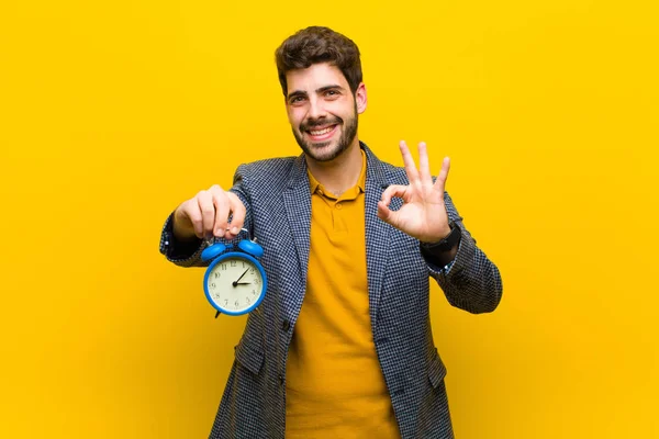 Young handsome man with an alarm clock against orange background — Stock Photo, Image