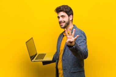 Bilgisayarı turuncu arka planda olan genç ve yakışıklı bir adam.
