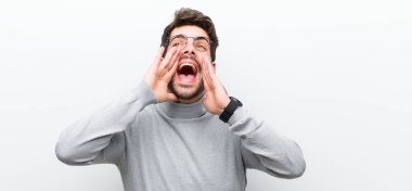 Genç menajer mutlu, heyecanlı ve pozitif hissediyor. Elleri ağızda, beyaz duvara doğru bağırıyor.