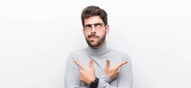 Genç yönetici şaşkın ve şaşkın görünüyor, güvensiz ve beyaz duvara karşı şüpheyle zıt yönleri işaret ediyor.