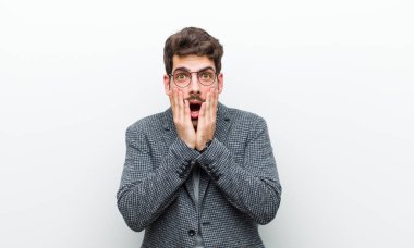 Genç müdür şok olmuş ve korkmuş hissediyor. Ağzı açık ve elleri beyaz duvarda.
