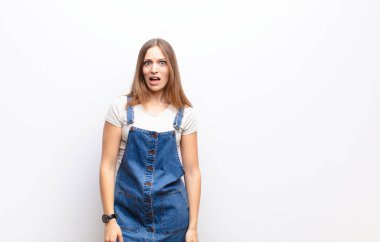 Genç, güzel bir kadın beyaz duvara karşı şaşkın, sinirli, sinirli ya da hayal kırıklığına uğramış gibi görünüyor.