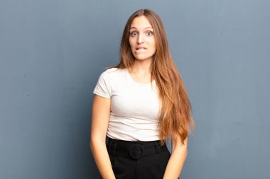 Genç, güzel bir kadın şaşkın ve kafası karışmış görünüyor. Gergin bir hareketle dudağını ısırıyor. Gri arka plandaki sorunun cevabını bilmiyor.