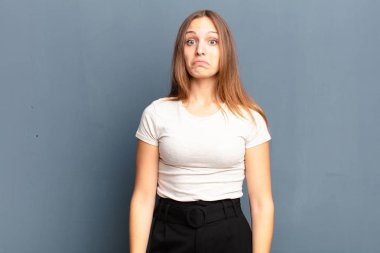 Genç, güzel bir kadın üzgün ve stresli. Kötü bir sürpriz yüzünden üzgün. Gri arka plana karşı olumsuz ve endişeli bir bakış.