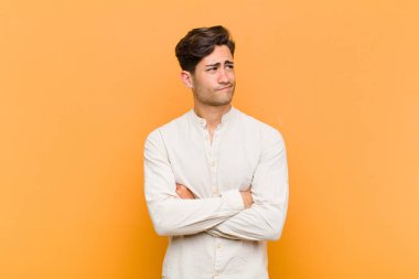 Endişeli, kafası karışık, budala bir ifadeyle genç yakışıklı adam, kopya alanı arıyor, turuncu arka plandan şüphe ediyor.