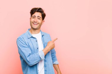 Genç ve yakışıklı adam heyecanlı ve şaşırmış görünüyor. Pembe arka plandaki boşluğu kopyalamak için yan ve yukarı işaret ediyor.