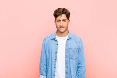 Genç yakışıklı adam şaşkın ve şaşkın görünüyor, gergin bir hareketle dudaklarını ısırıyor, pembe arka plandaki sorunun cevabını bilmiyor.