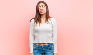 Genç, güzel bir kadın endişeli, stresli, endişeli ve korkmuş görünüyor. Pembe arka plana karşı panikliyor ve dişlerini sıkıyor..