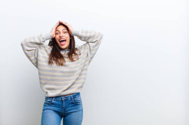 Genç ve güzel bir kadın el ele tutuşuyor, ağzı açık, son derece şanslı, şaşkın, heyecanlı ve mutlu, beyaz duvara karşı izole edilmiş.