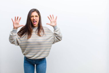 Genç, güzel bir kadın panik ya da öfke içinde çığlık atıyor. Şok olmuş, korkmuş ya da öfkeli. Elleri başının yanında beyaz duvara yaslanmış.