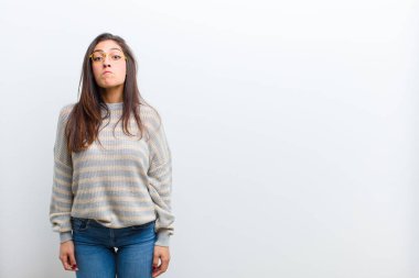 Genç ve güzel bir kadın üzgün ve stresli, kötü bir sürpriz yüzünden üzgün, olumsuz, endişeli bir bakışla beyaz duvara yaslanmış