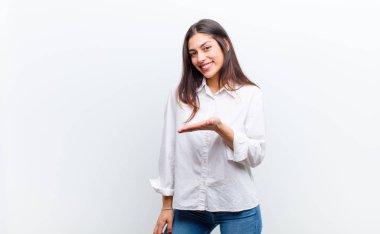 Genç, güzel bir kadın neşeyle gülümsüyor, mutlu hissediyor ve fotokopi odasında bir konsept gösteriyor. Avuç içi beyaz duvara yaslanmış.