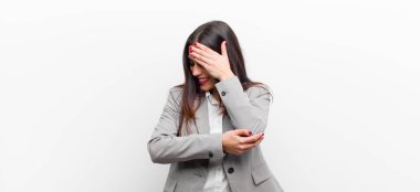 Genç, güzel bir kadın stresli, utanmış ya da üzgün görünüyor. Başı ağrıyor, yüzü beyaz duvara yaslanmış.