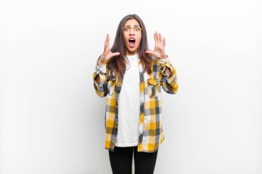 Genç ve güzel bir kadın ellerini havaya kaldırarak çığlık atıyor. Öfkeli, sinirli ve üzgün hissediyor. Beyaz duvara yaslanmış.