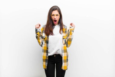 Genç ve güzel bir kadın öfkeli bir ifadeyle bağırıyor ya da yumruklarıyla başarıyı kutluyor. Beyaz duvara karşı izole edilmiş.