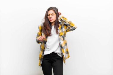 Genç ve güzel bir kadın stresli, hayal kırıklığına uğramış ve yorgun hissediyor. Endişeli ve sorunlu bir bakışla beyaz duvara yaslanmış bir şekilde boynu okşuyor.