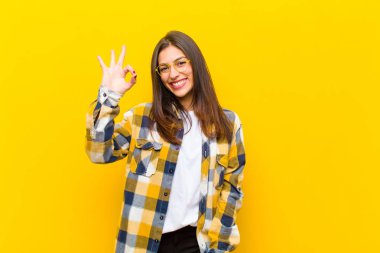 Genç, güzel bir kadın kendini mutlu, rahat ve tatmin olmuş hissediyor. Onayını iyi bir hareketle gösteriyor. Turuncu duvara gülümsüyor.