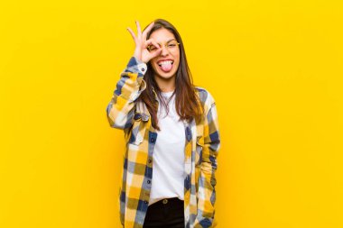 Genç ve güzel bir kadın mutlu bir şekilde gülümsüyor, şaka yapıyor ve gözetleme deliğinden bakıyor, turuncu duvara karşı sırları gözetliyor.