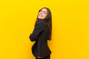 Genç, güzel bir kadın neşeyle gülümsüyor, mutlu, tatmin olmuş ve rahatlamış hissediyor, kollarını kavuşturup turuncu duvara bakıyor.