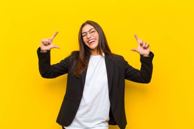 Genç, güzel bir kadın kendi gülümsemesini çerçeveliyor ya da iki eliyle özetliyor. Olumlu ve mutlu görünüyor. Turuncu duvara karşı sağIık kavramı.