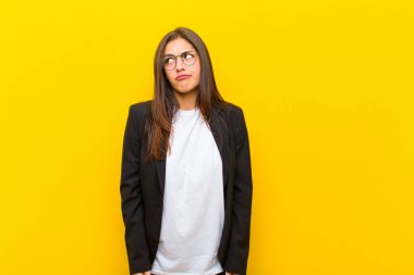 Genç ve güzel bir kadın şaşırmış ve kafası karışmış görünüyor. Bir sorunu çözmeye çalışıyor ya da turuncu duvara karşı düşünüyor.