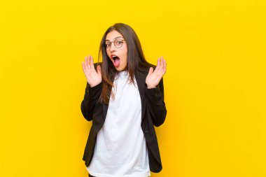 Genç, güzel bir kadın turuncu duvara karşı inanılmaz bir şey fark edince şaşırmış ve şaşırmış görünüyor.