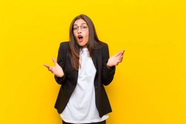 Genç ve güzel bir kadın ağzı açık ve şaşırmış, şaşırmış ve şaşırmış turuncu duvara karşı inanılmaz bir sürprizle