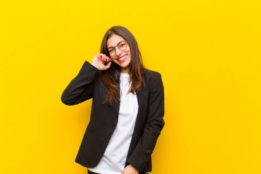 Genç, güzel bir kadın turuncu duvarın karşısında neşeli ve kendinden emin bir şekilde gülüyor.