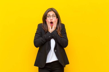 Genç ve güzel bir kadın hoş olmayan bir şekilde şok olmuş, korkmuş ya da endişeli görünüyor. Ağzı sonuna kadar açık ve iki kulağını da turuncu duvara dayamış.