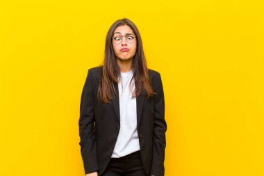 Genç ve güzel bir kadın aptal ve komik görünüyor. Aptal şaşı bir ifadeyle, şakalaşıyor ve turuncu duvarda oynaşıyor.