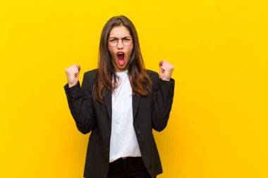 Genç ve güzel bir kadın sinirli bir ifadeyle ya da turuncu duvara karşı başarıyı kutlayan yumruklarla agresif bir şekilde bağırıyor.