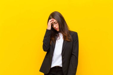 Genç ve güzel bir kadın stresli, mutsuz ve hayal kırıklığına uğramış, alnına dokunuyor ve turuncu duvara karşı şiddetli baş ağrısı çekiyor.