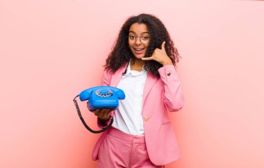 Pembe duvar arkasında klasik bir telefonu olan genç siyah güzel bir kadın.
