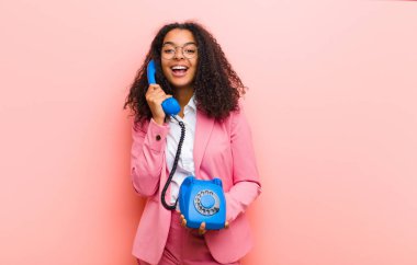 Pembe duvar arkasında klasik bir telefonu olan genç siyah güzel bir kadın.
