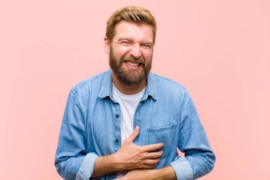 Genç sarışın yetişkin bir adam komik bir şakaya gülüyor, mutlu ve neşeli hissediyor, eğleniyor.