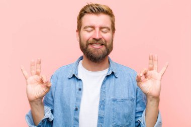 Genç sarışın yetişkin bir adam konsantre olmuş ve meditasyon yapıyor, kendini tatmin olmuş ve rahatlamış hissediyor, düşünüyor ya da bir seçim yapıyor.